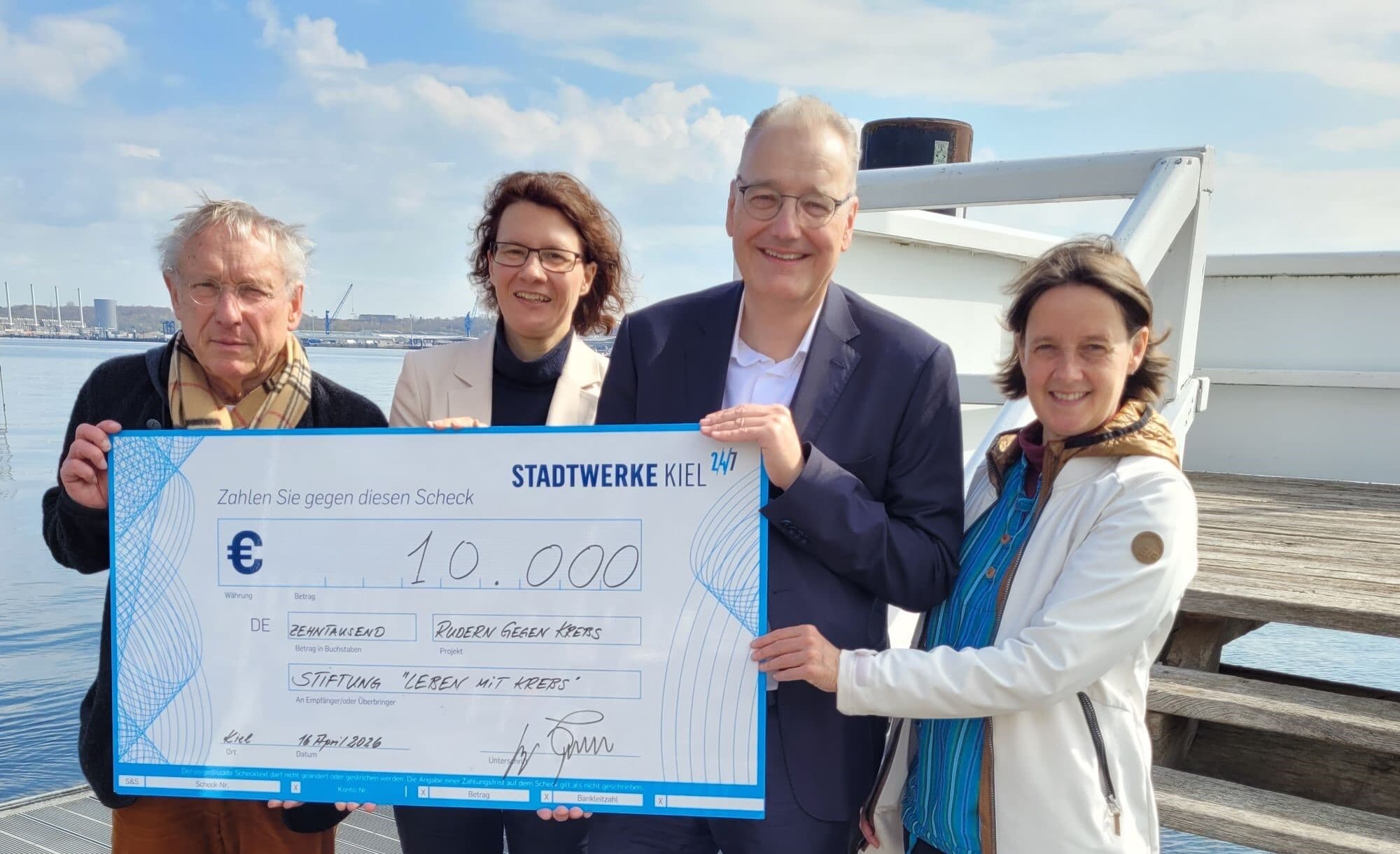 Scheckübergabe Rudern gegen Krebs. 4 Menschen, die sich über den Scheck freuen. Auf dem Bild zu sehen sind von links nach rechts: Rolf Kalippe, Nicole Schröder, Dr. Teupen, Maja Darmstadt