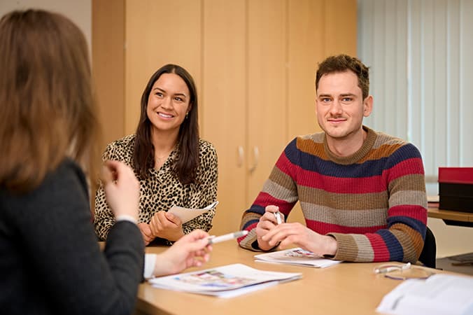 Zwei Frauen und ein Mann sitzen in einem Personalgespräch zusammen und der Mann schaut in die Kamera.