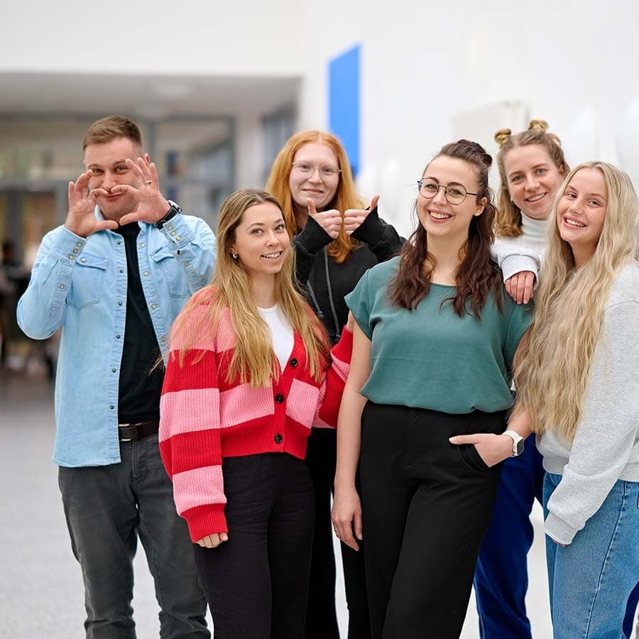 Eine Gruppe von Auszubildenen umringt ihre Lehrerin auf dem Flur des SKK Bildungszentrums und alle lächeln in die Kamera.